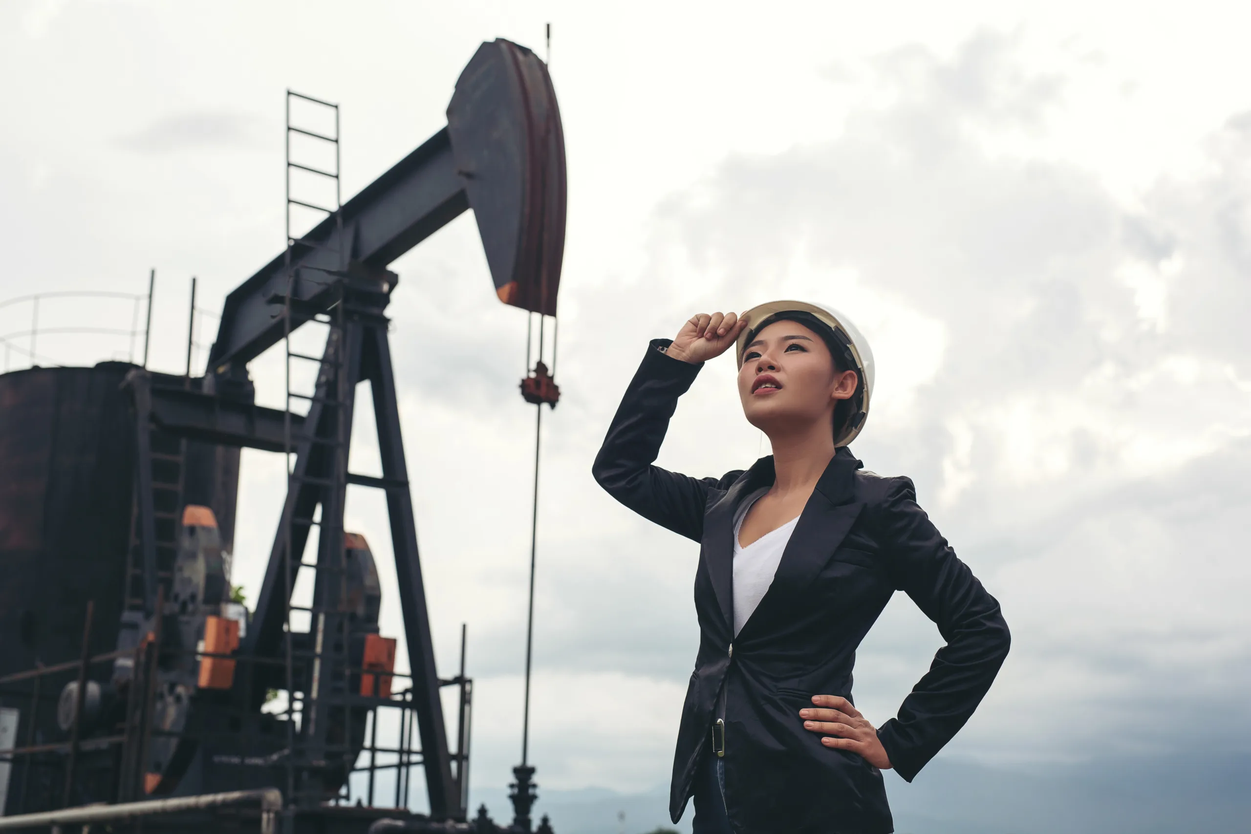 female-engineer-standing-with-working-oil-pumps-with-white-sky